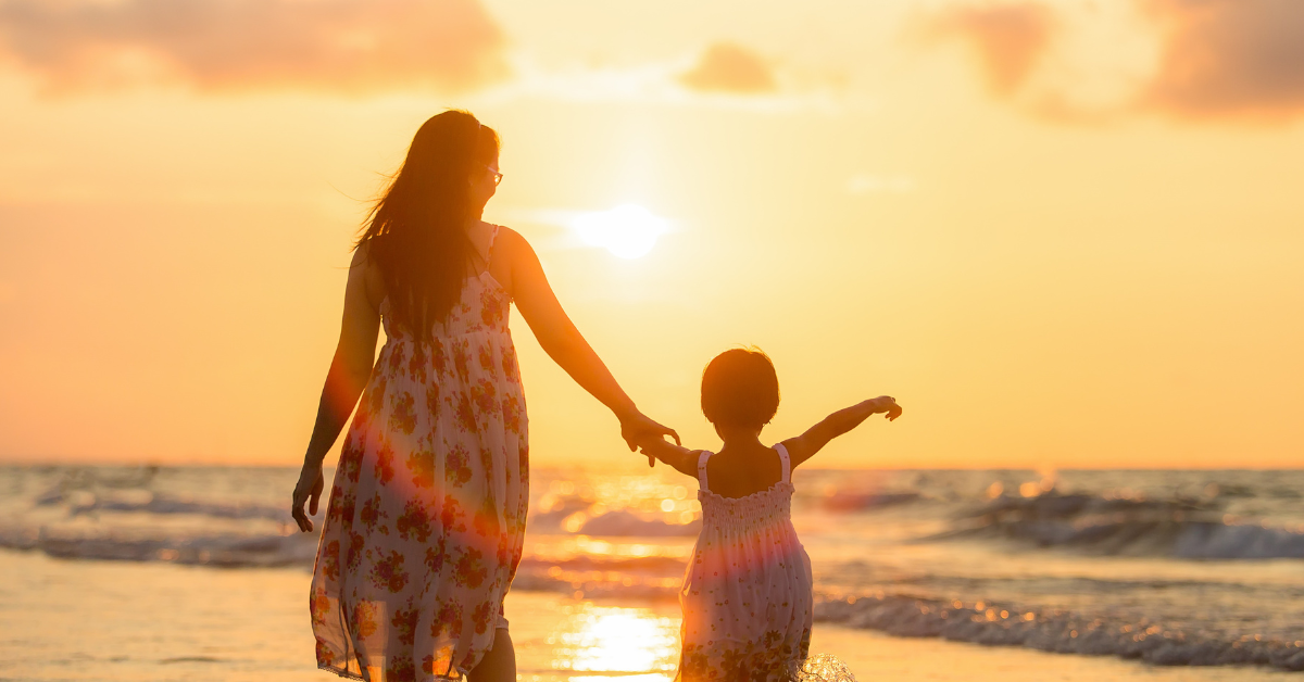 Mothers and Mother’s Day - Mother and child walking on the beach holding hands at sunset